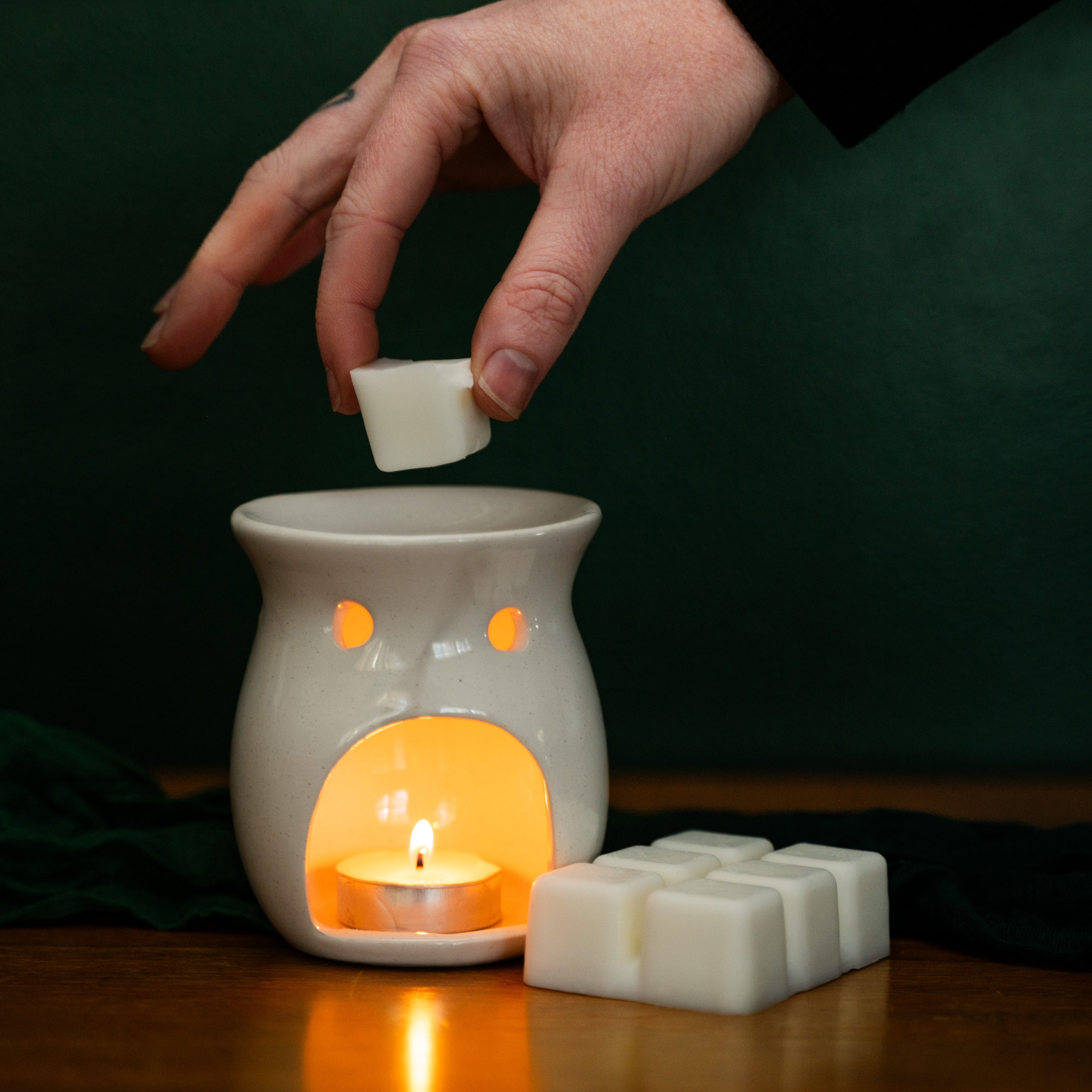 Hand placing a wax melt into a white wax warmer with a dark background